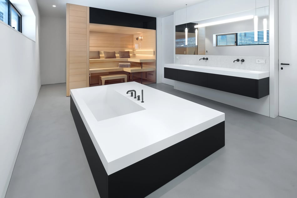 Modernes-Spa-mit-grosser-Badewanne-und-Waschtisch-aus-weiss-schwarzem-Mineralwerkstoff-und-integrierter-Sauna