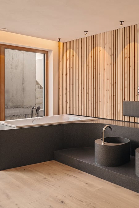 Moderner-Spa-Bereich-mit-Badewanne-und-Waschbecken-aus-dunklem-Mineralwerkstoff-und-holzverkleideten-Waenden