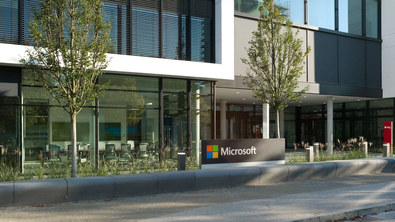 Microsoft-Logo-vor-Gebaeudekomplex-mit-Konferenzraum-hinter-der-Glasfront-V1