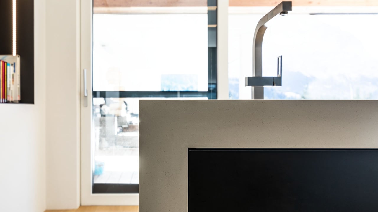 Detail-der-dicken-Arbeitsflaeche-in-Betonoptik-mit-Wasserhahn-und-Fenster-im-Hintergrund