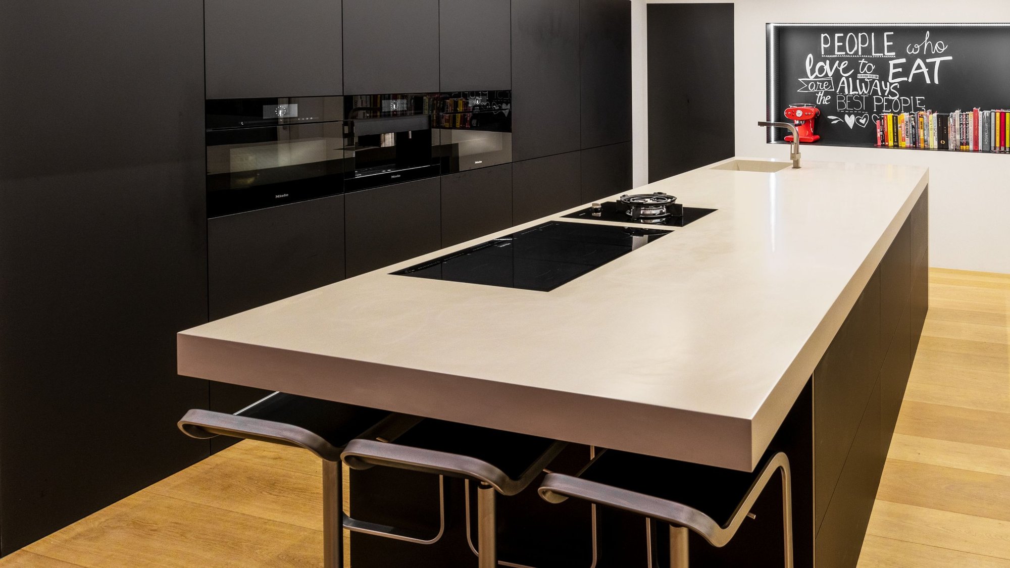 Kuecheninsel-Betonoptik-mit-eingelassenem-Kochfeld-und-Barhockern-davor-Querformat