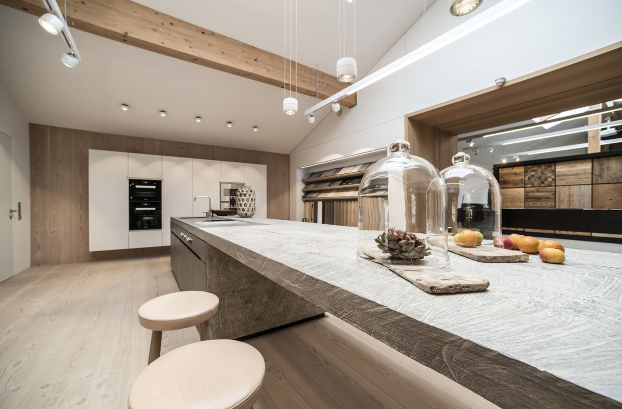 Moderne-Kueche-mit-Kochinsel-in-grauer-Betonoptik-heller-Holzdecke-und-offenem-Raumkonzept