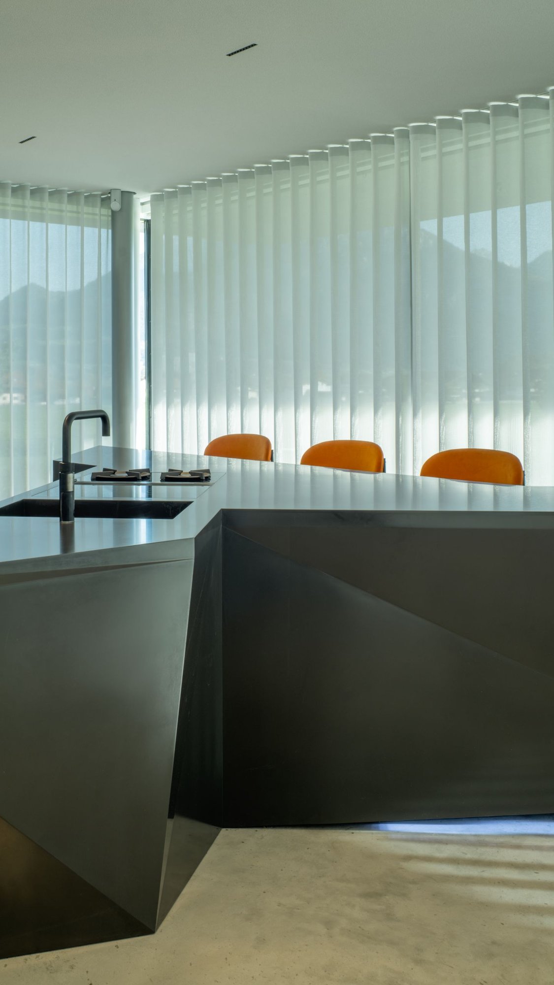 Diamantfoermige-dunkle-Kuecheninsel-mit-integrierter-Spuele-und-Hahn-drei-orange-Sitze-hinter-dem-Tresen Diamantfoermige-dunkle-Kuecheninsel-mit-integrierter-Spuele-und-Hahn-drei-orange-Sitze-hinter-dem-Tresen