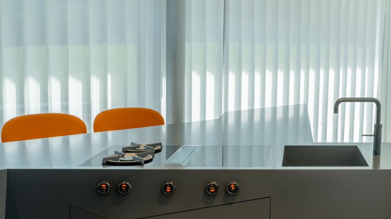 Kochbereich-der-dunklen-Kuecheninsel-mit-Gasbrennern-und-Wasserhahn-vor-einem-hohen-Fenster-mit-Vorhang