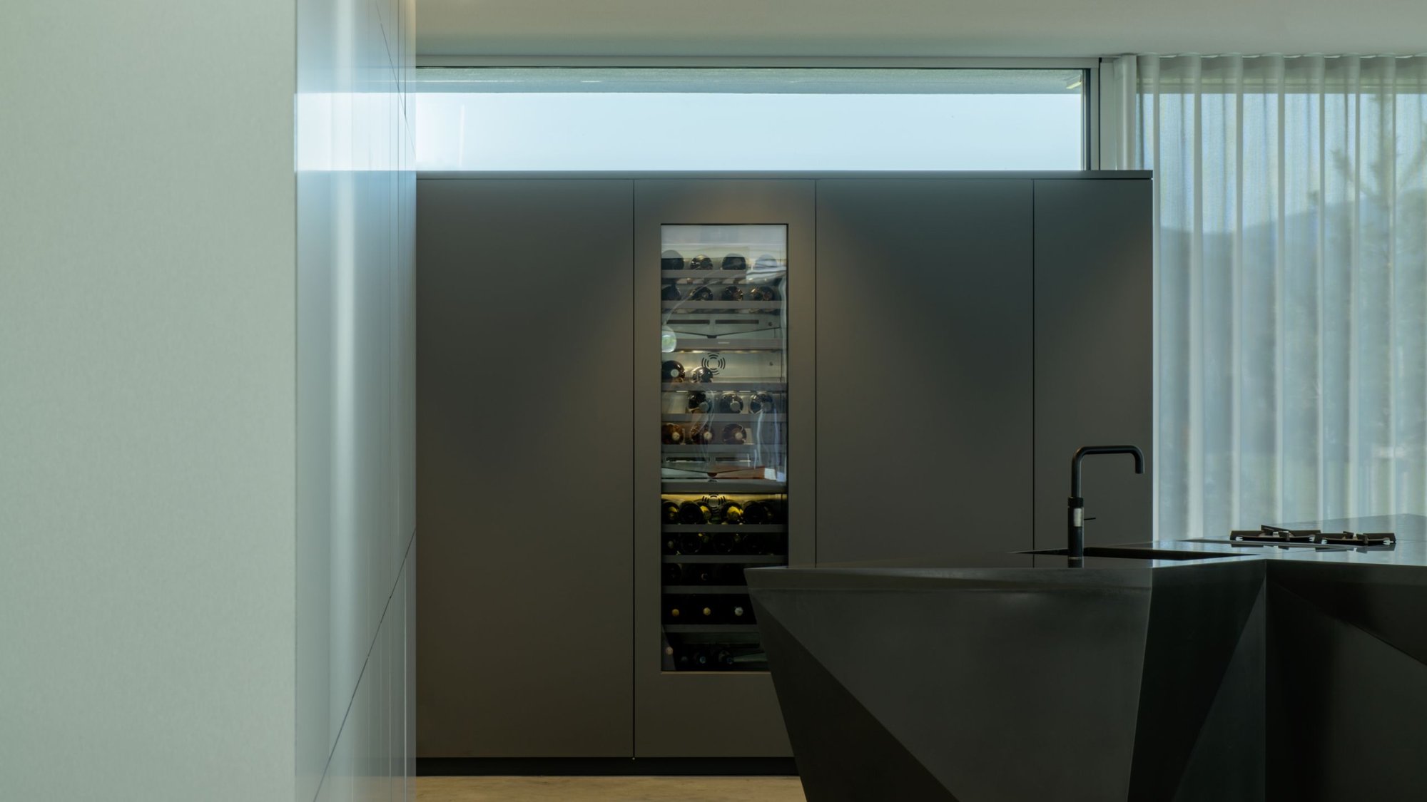 Moderne-Kueche-mit-dunkler-diamantfoermiger-Insel-und-integriertem-WeinKuehlschrank-hinter-Glasfront Moderne-Kueche-mit-dunkler-diamantfoermiger-Insel-und-integriertem-WeinKuehlschrank-hinter-Glasfront