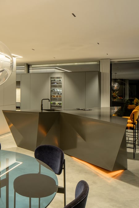 Polygonale-Kuecheninsel-aus-dunklem-Mineralwerkstoff-in-moderner-Wohnumgebung-mit-Designbeleuchtung