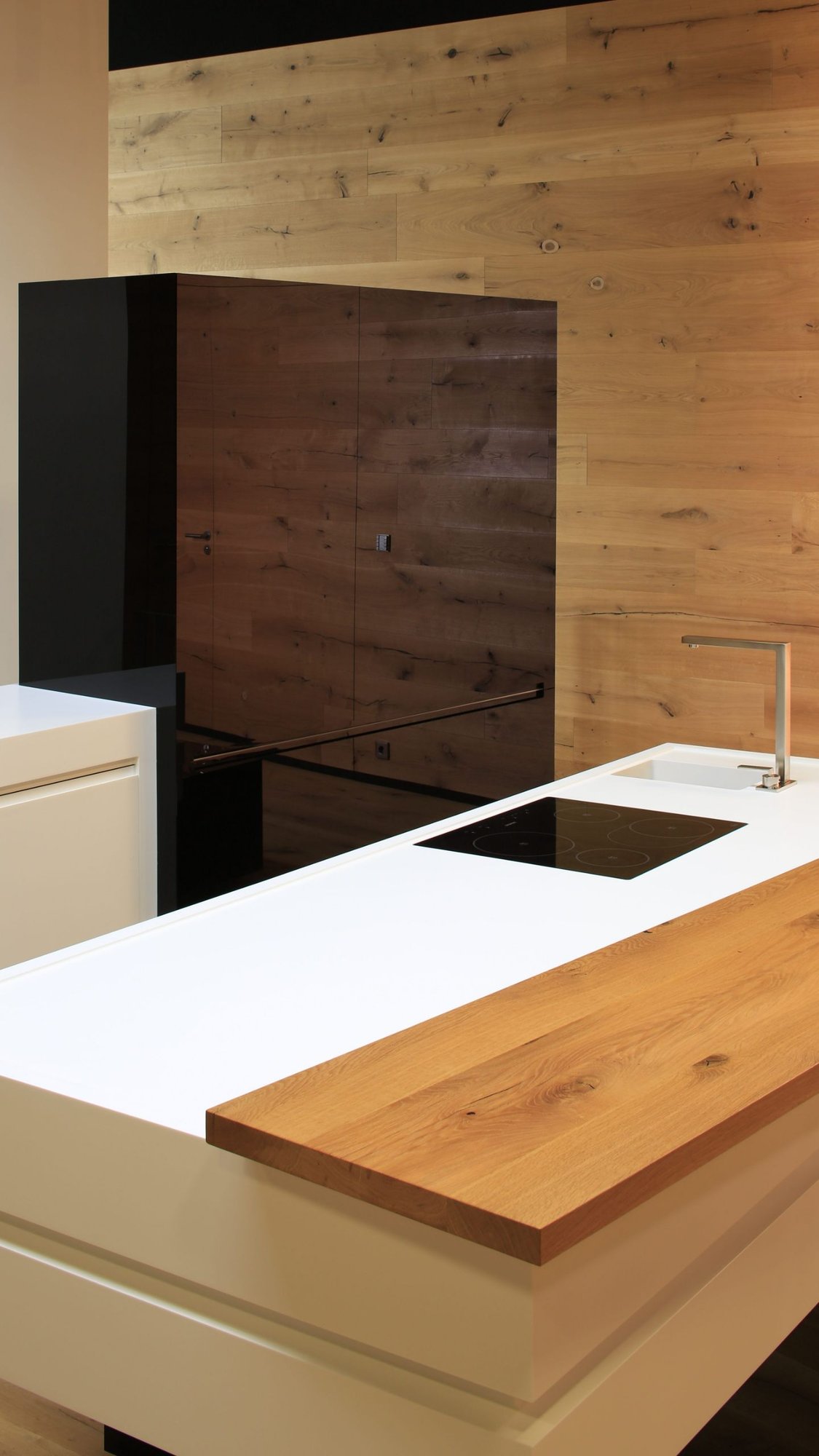 Detail-der-weissen-Corian-Arbeitsplatte-mit-Holzelement-und-induktionskochfeld-vor-Holz-Wandverkleidung