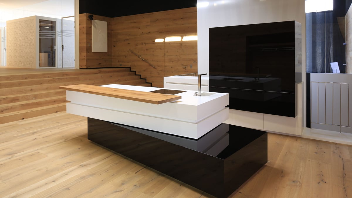 Schwebende-Kuecheninsel-mit-weisser-Corian-Platte-und-schwarzem-Hochglanz-Sockel-in-Holzumgebung