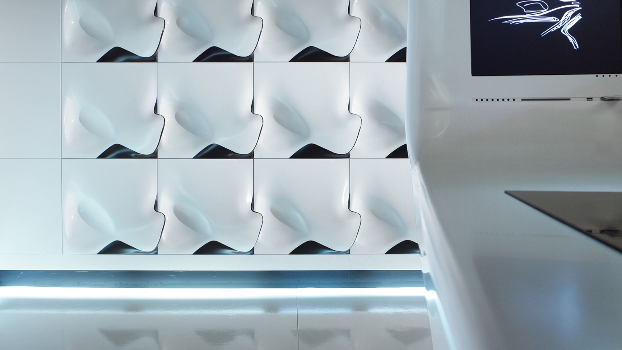 Detailansicht-der-skulpturalen-Wandverkleidung-bestehend-aus-kachelartigen-tief-gefraesten-und-thermisch-verformten-Corian-Paneelen-mit-wellenartiger-3D-Struktur Detailansicht-der-skulpturalen-Wandverkleidung-bestehend-aus-kachelartigen-tief-gefraesten-und-thermisch-verformten-Corian-Paneelen-mit-wellenartiger-3D-Struktur