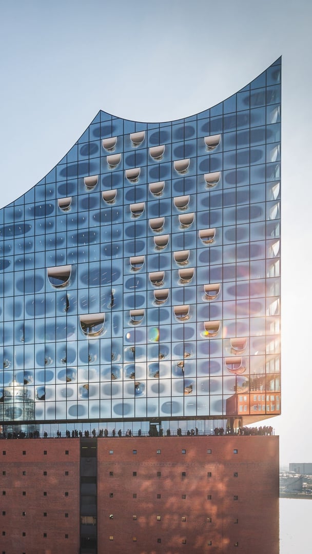 Sonnenbeschienene-Aussenansicht-der-Elbphilharmonie-Hamburg-mit-der-wellenfoermigen-Glasfassade-und-dem-roten-Backsteinsockel