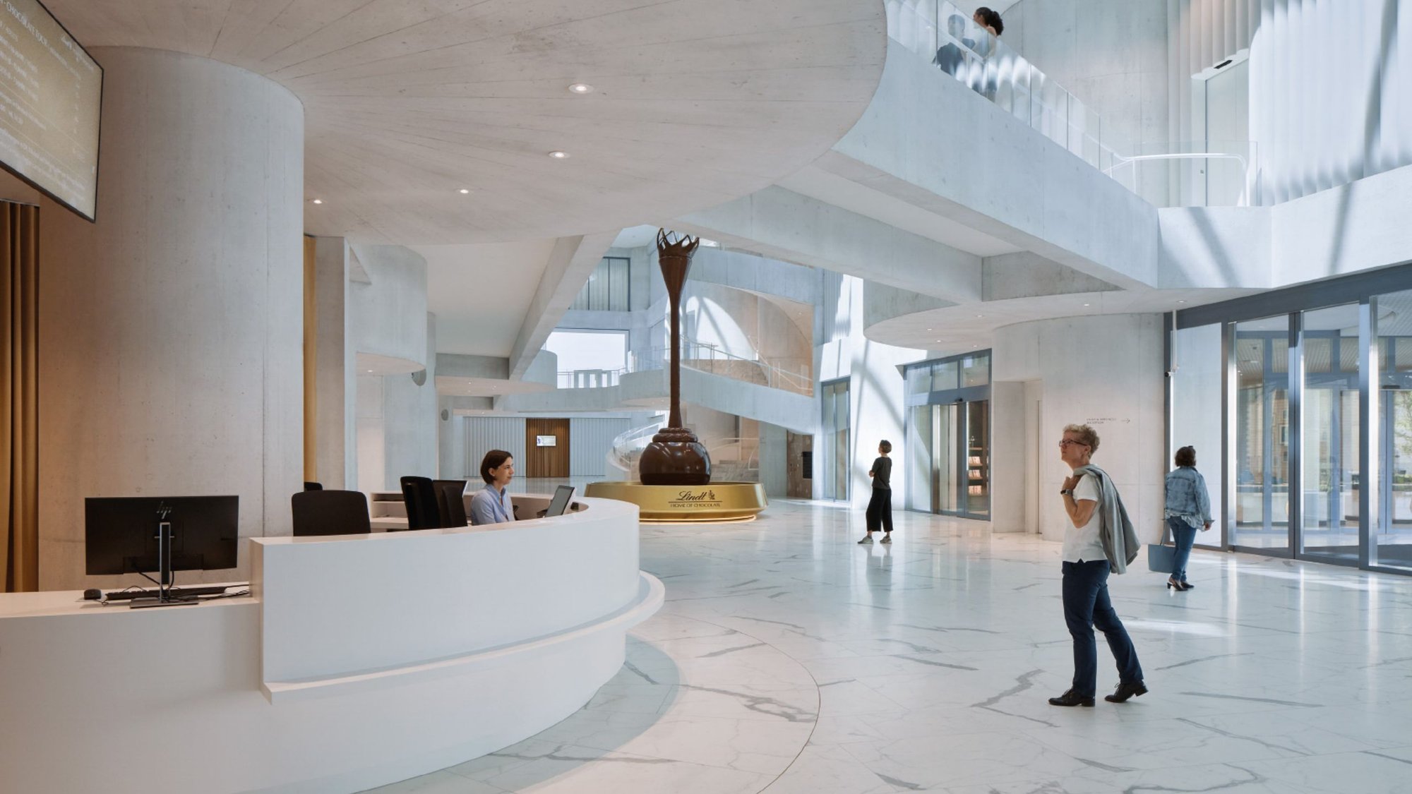 Empfangsbereich-mit-Mitarbeiterin-und-Schokoladenbrunnen-im-Lindt-Home-of-Chocolate Empfangsbereich-mit-Mitarbeiterin-und-Schokoladenbrunnen-im-Lindt-Home-of-Chocolate