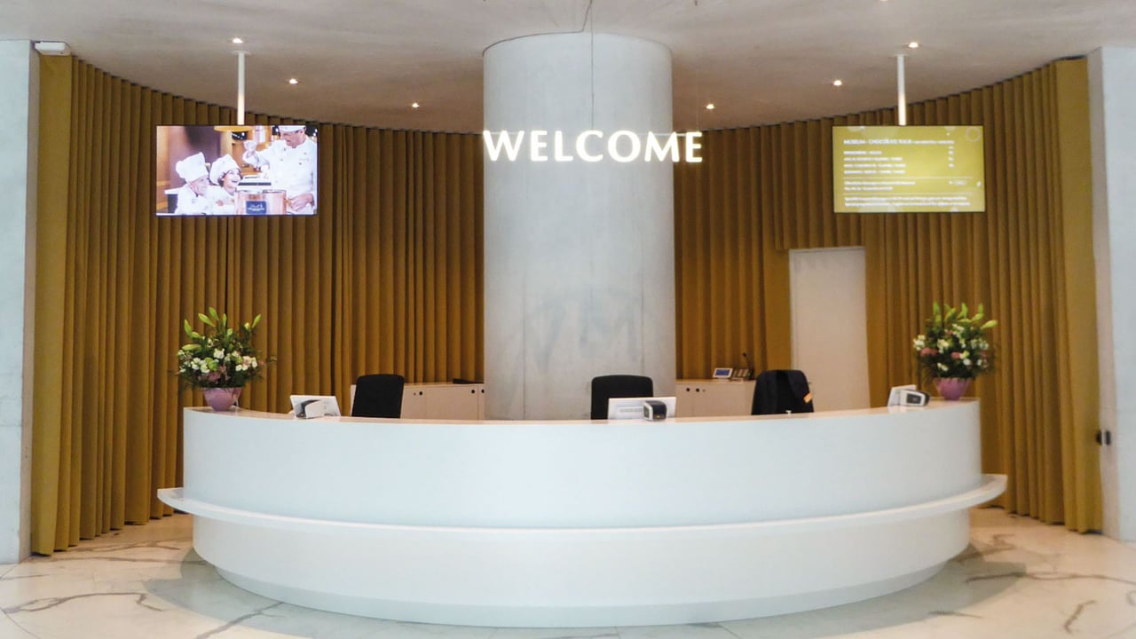 runde-weiße-Empfangstheke-mit-Welcome-Schriftzug-und-goldenen-Vorhängen-im-Lindt-Home-of-Chocolate