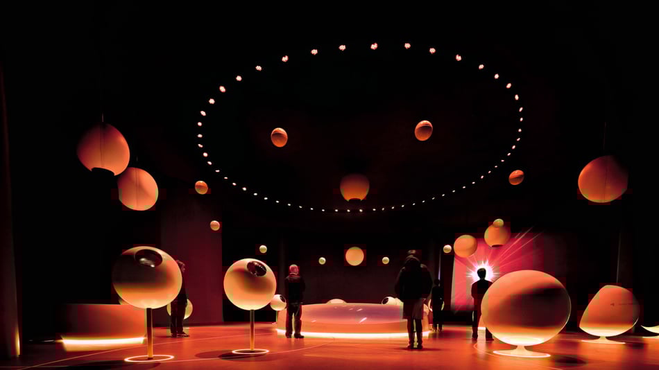 Besucher in der Cern futuristischen Ausstellung mit großen leuchtenden Kugeln und dunklem Raum