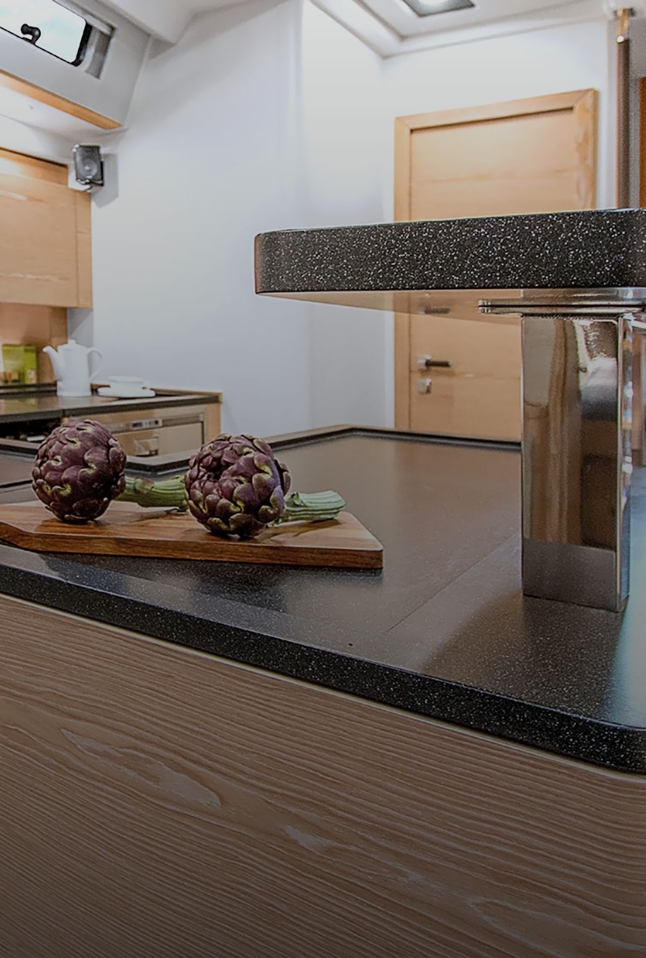 Kueche-im-Schiff-mit-Arbeitsplatte-aus-dunklem-Mineralwerkstoff-und-Artischocken-auf-Schneidebrett