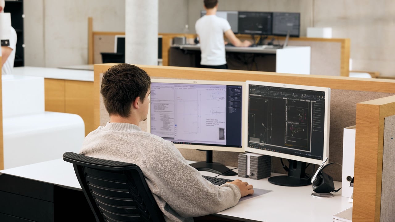 Mitarbeiter-in-der-Planungsabteilung-arbeitet-an-zwei-Bildschirmen-mit-technischen-Zeichnungen-fuer-die-Fertigung