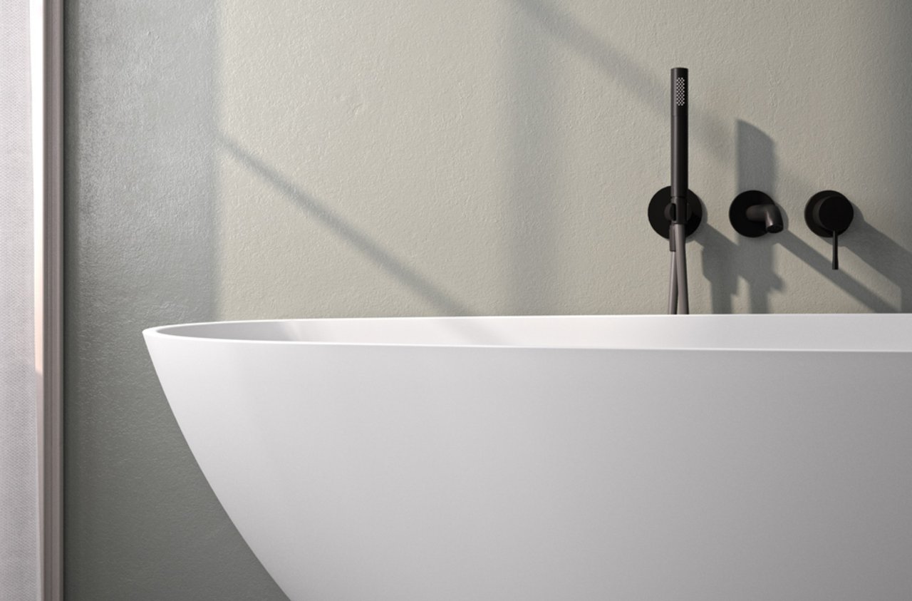 Freistehende-Badewanne-aus-weissem-Mineralwerkstoff-mit-schwarzer-Armatur-vor-heller-Wand
